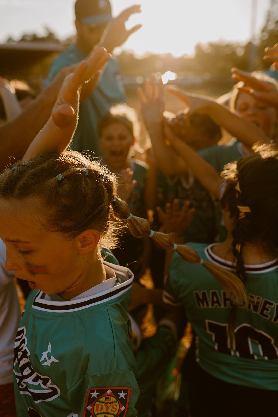 Bluffton All-Star players raising their hands together in a team huddle at sunset